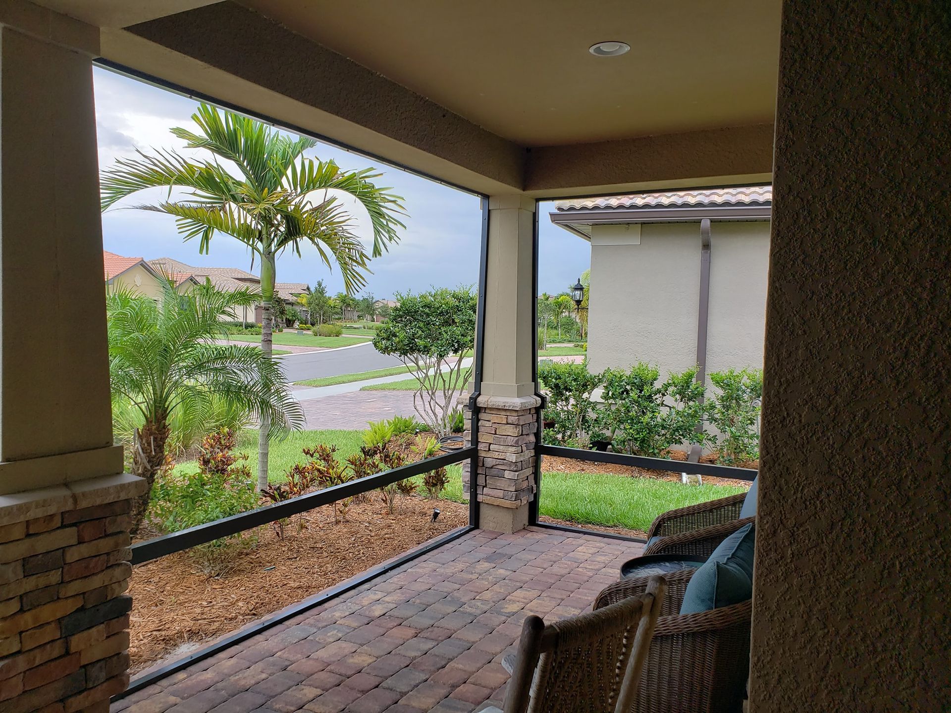 Covered porch with screens, brick flooring, and view of a street, palm trees, and houses.