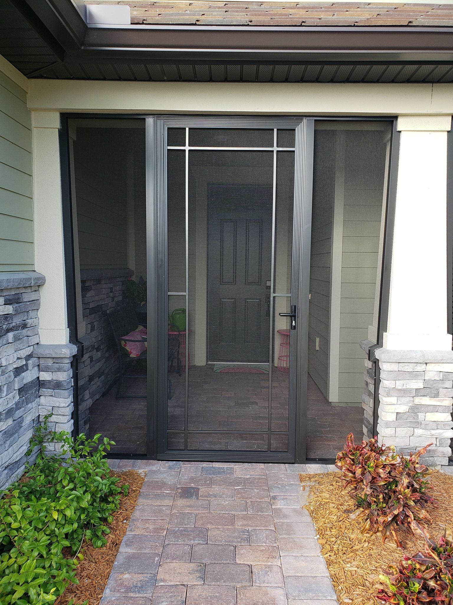 Black screen door open, revealing a brick pathway, plants, and the interior doorway.