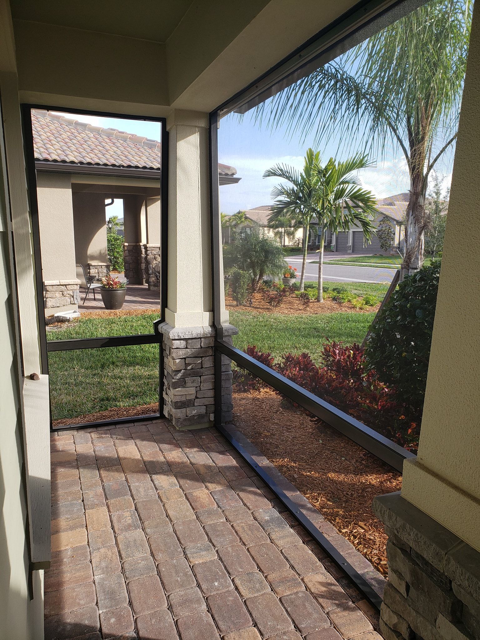 Screened porch with brick pavers, view of a yard and street beyond the screen.