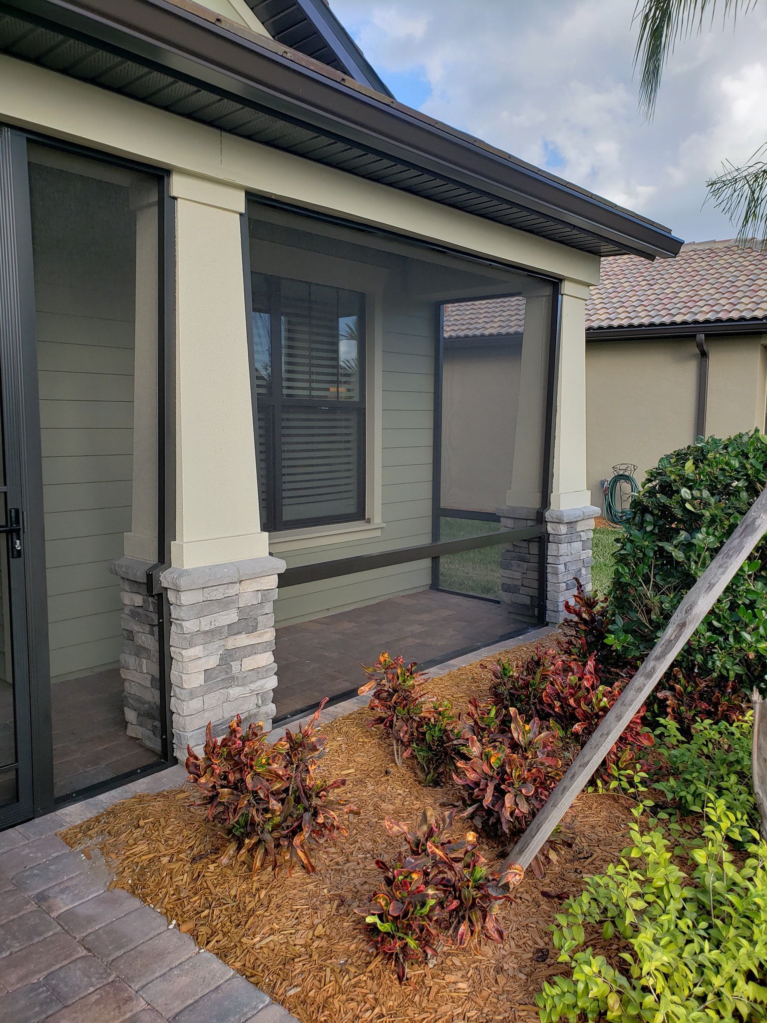 Screened porch with stone columns and landscaping; neutral-toned exterior, dark-framed screens.