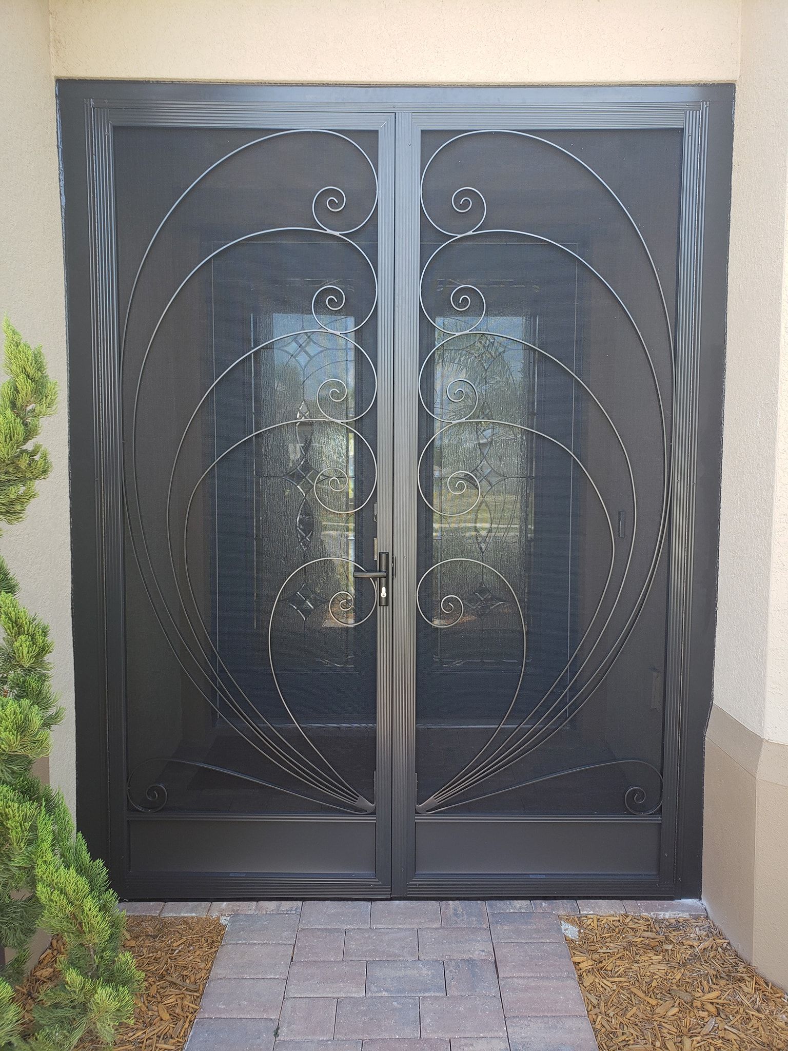 Black, ornate security doors with decorative metalwork. Stone pathway leads to the entrance.