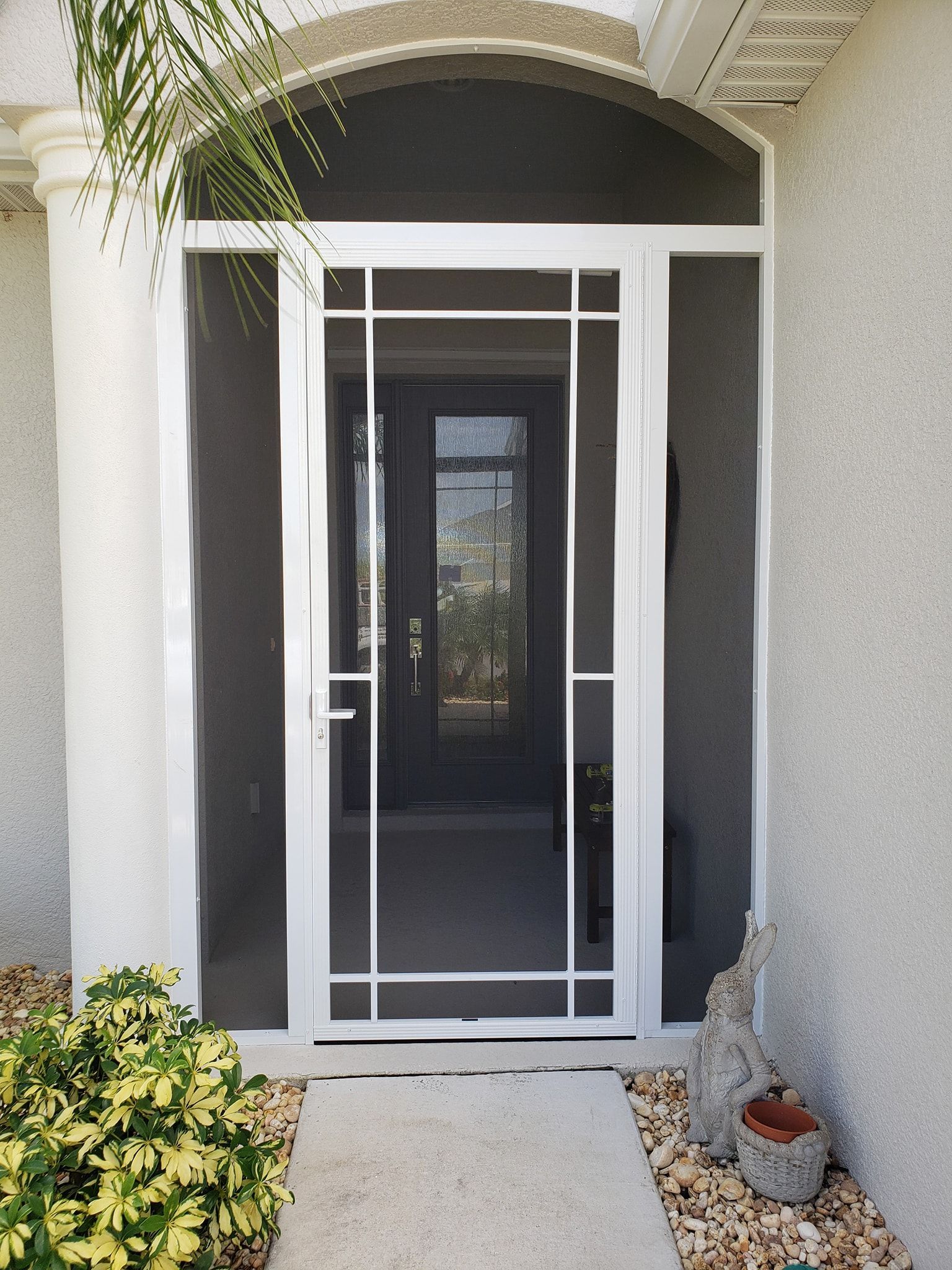 White screen door with sidelights, covering a front door on a light stucco house.