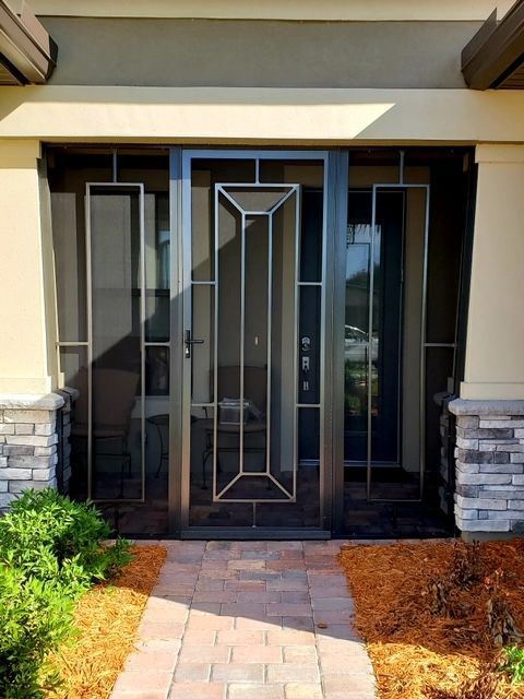 Black metal screen door with side panels, on a brick pathway, next to a beige stucco and stone exterior.
