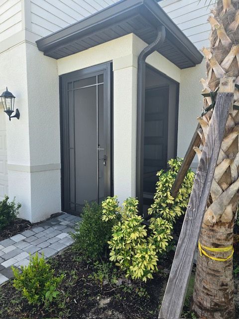 Exterior view of a house entry with a dark screen door, a small garden, and a walkway.