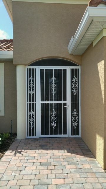Exterior doorway with white security screen door, decorative metal grillwork, brick walkway.