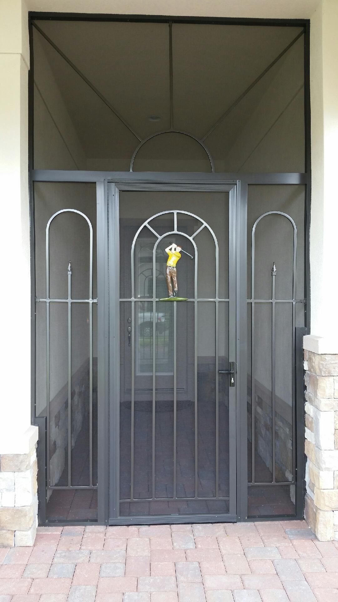 Black metal screen door with golf figure, set against brick and beige exterior.