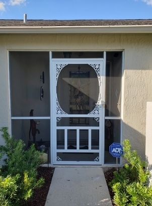White screen door with decorative filigree, flanked by screen panels, leading to a home's entryway.