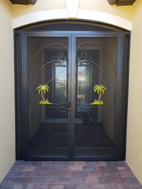 Black double screen doors with ornate metalwork, featuring palm tree accents, set in a light tan doorway.