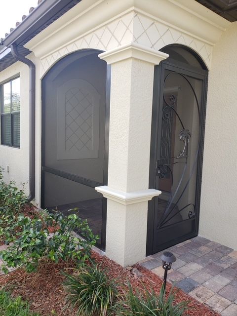Beige stucco entrance with screen door, arched doorway, and column.