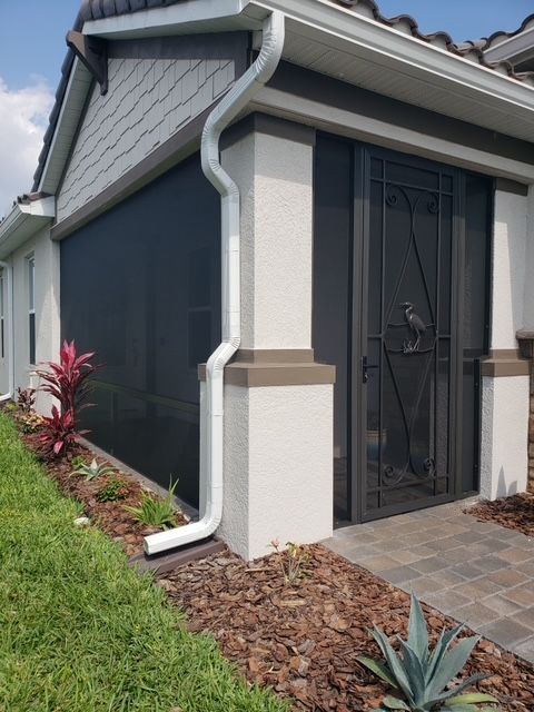 Exterior of house with screened porch and black screen. White pillars, white gutter, and landscaping.