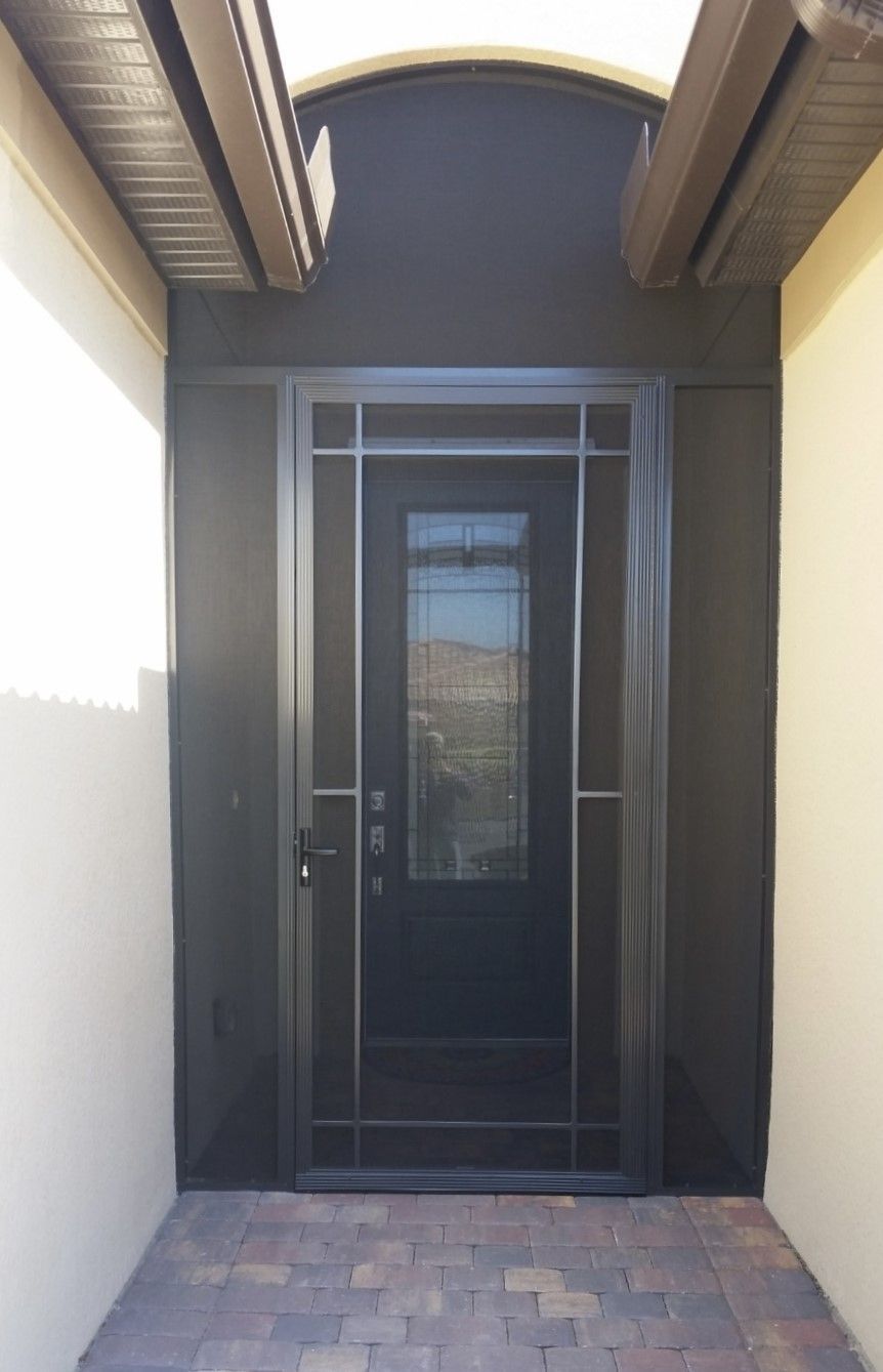 Black framed entry door with screen. Exterior with brick patio, black trim, and beige walls.