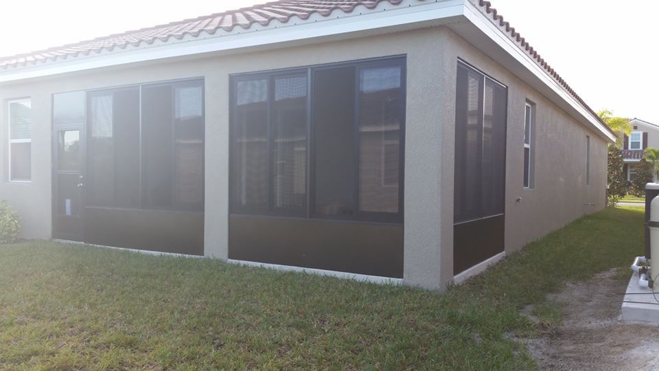 Exterior view of a beige house with black-framed screened-in windows and a green lawn.