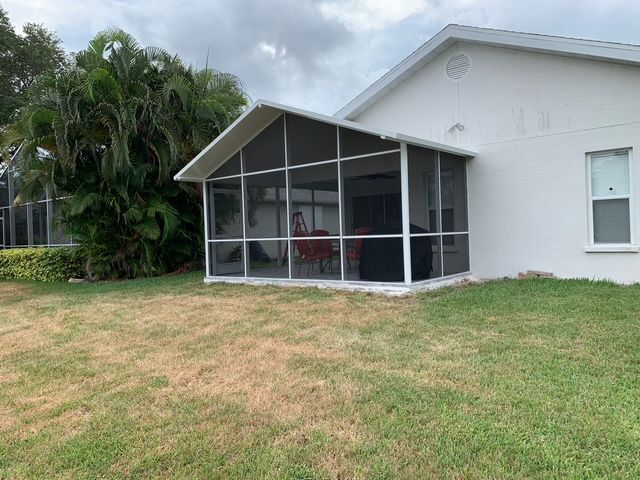 White screened-in porch attached to a white house with brown grass lawn.