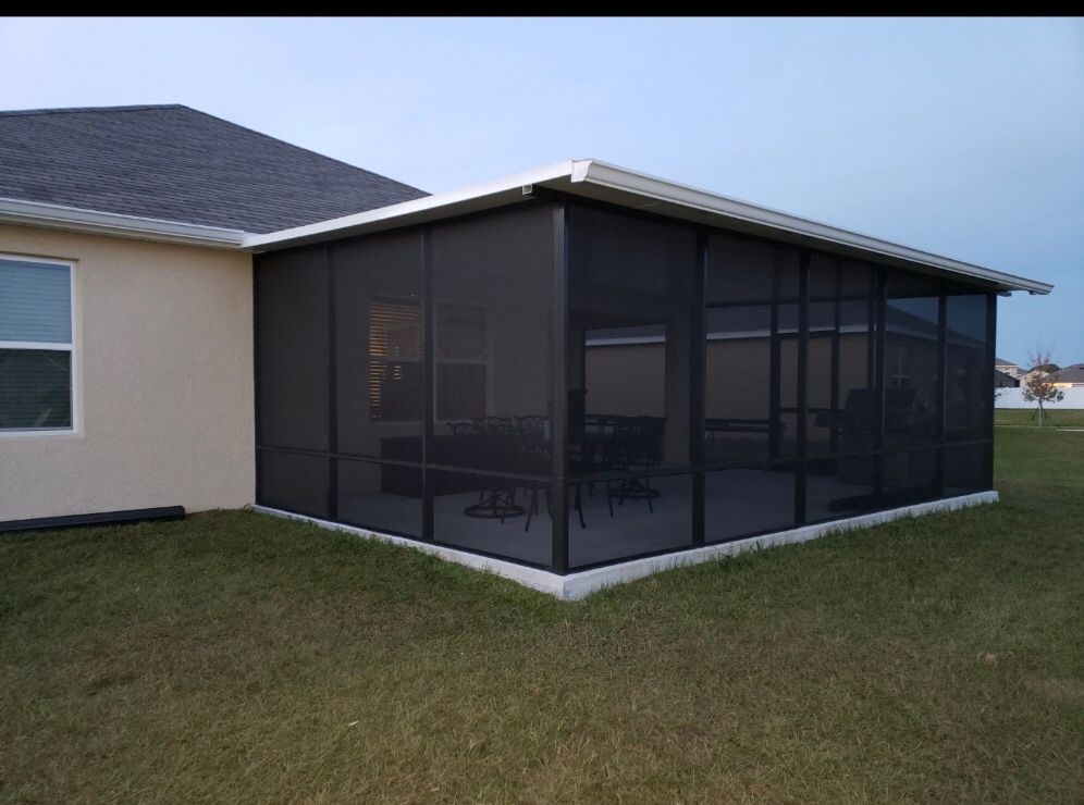 A screened-in porch attached to a light-colored house with dark screens, set on grass.