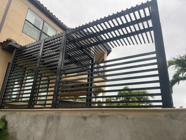 Black metal pergola attached to a beige building with horizontal and vertical bars.