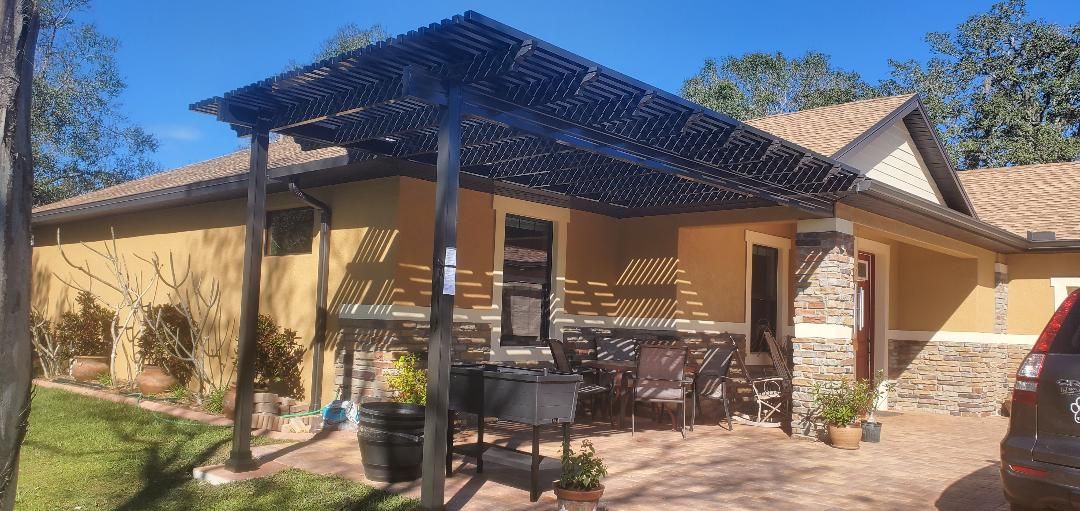 A one-story house with a wooden pergola over the entrance, with a brown roof and a car parked to the side.