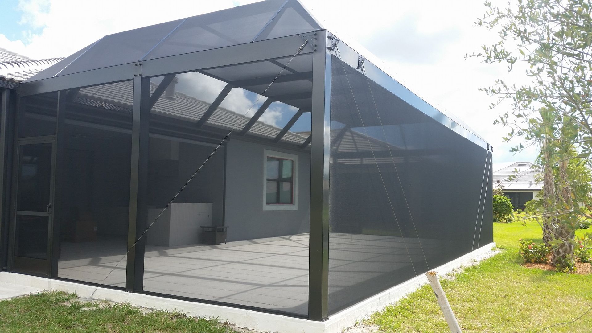 Screened-in patio enclosure with dark frame, glass roof panels, and a concrete patio.