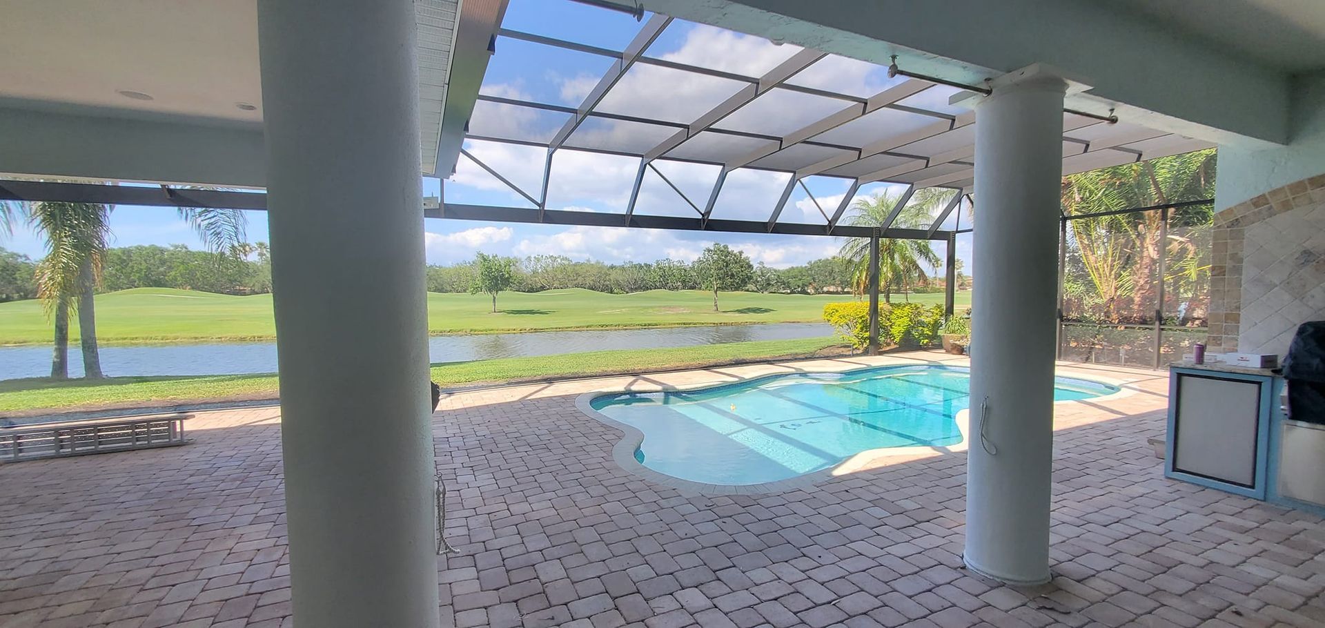 Patio with pool overlooking a golf course. White columns, blue sky, and green grass.