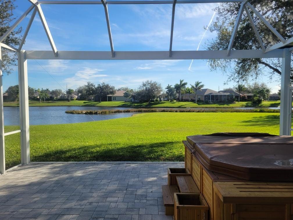 Patio with hot tub overlooking a lake and green lawn on a sunny day.
