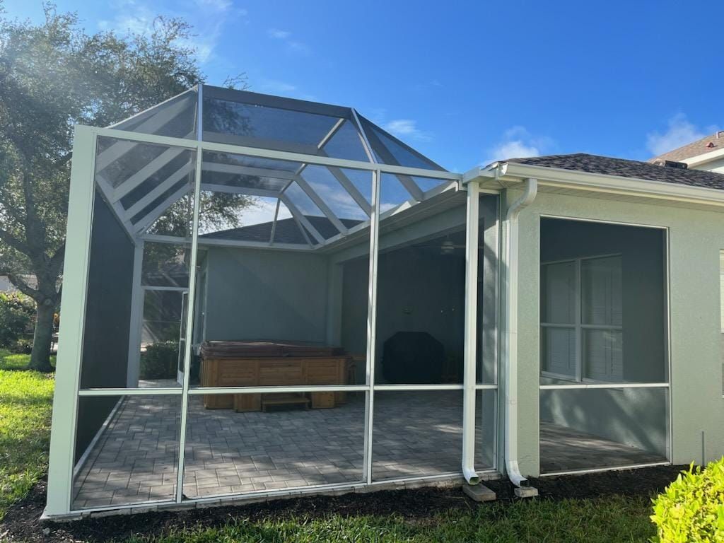 Screened-in patio with light-colored framing. Includes a brick paver floor, hot tub, and a connected house.