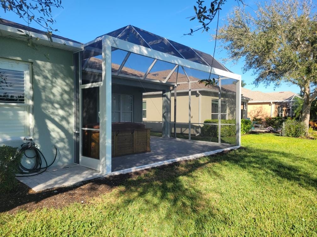 Screened patio addition attached to a house with a concrete patio and a lush green lawn.