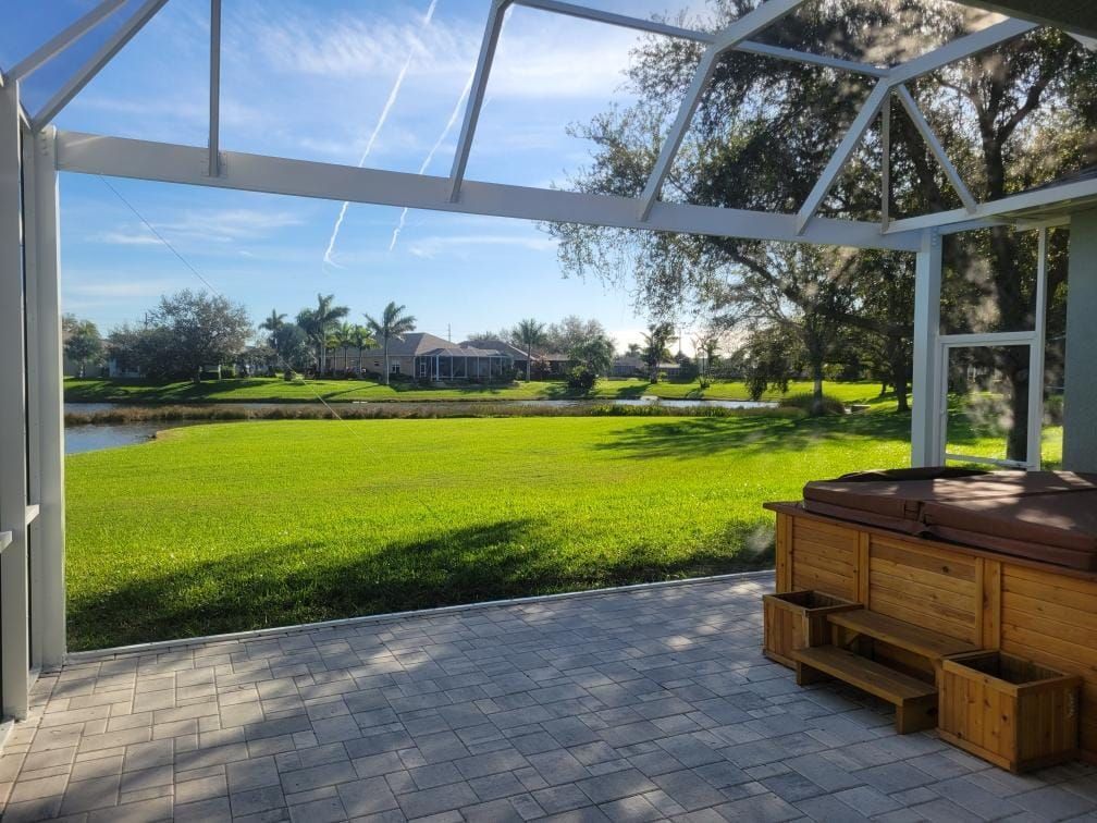 Patio with hot tub overlooking green lawn and lake, under a screened enclosure, sunny day.