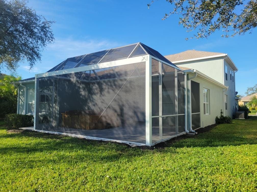 Screened porch attached to a two-story house with green lawn under a blue sky.