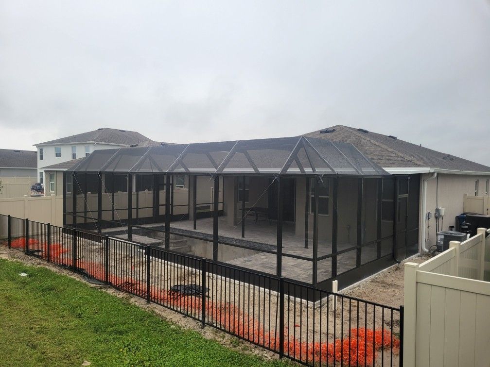 Screened-in pool enclosure attached to a house with a black metal fence and lawn in the foreground.