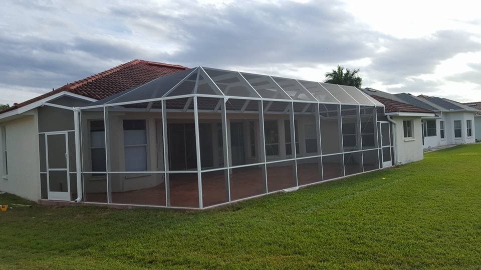 Screened-in patio extension attached to a white house with red tile roof, on green grass under cloudy sky.