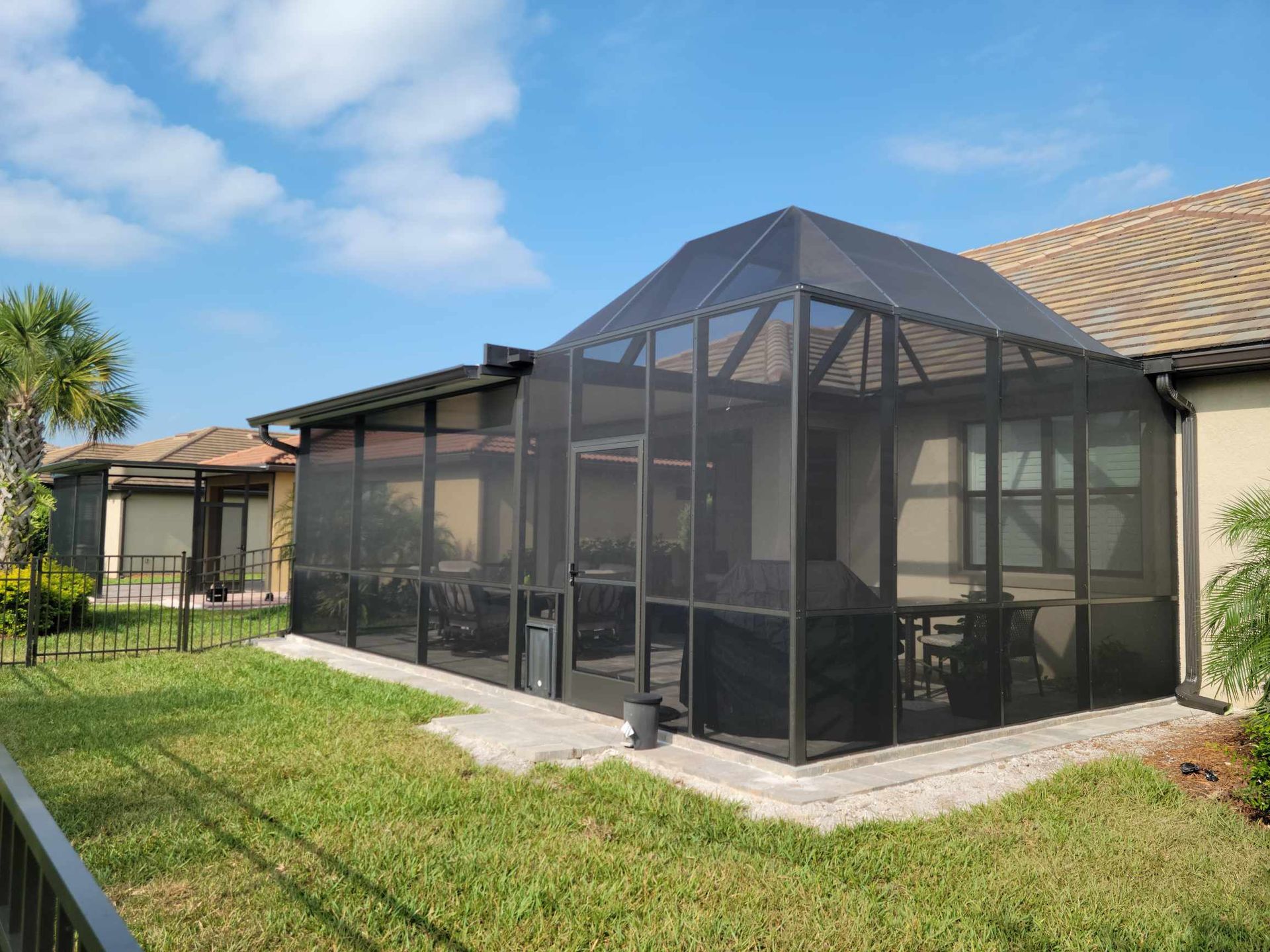 A screened-in porch attached to a beige house, with a green lawn and blue sky.
