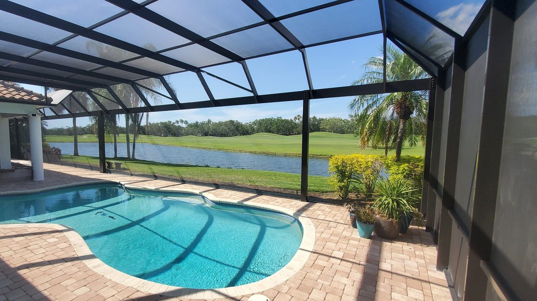 Screened-in pool area with view of golf course and water under a blue sky.