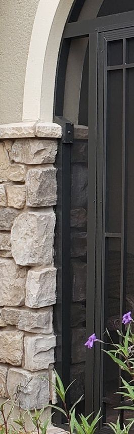 Stone column next to a black metal fence with purple flowers and greenery at the base.