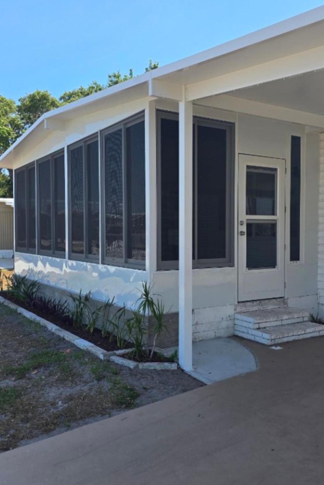White house with a screened porch and door, gray trim, and concrete walkway.