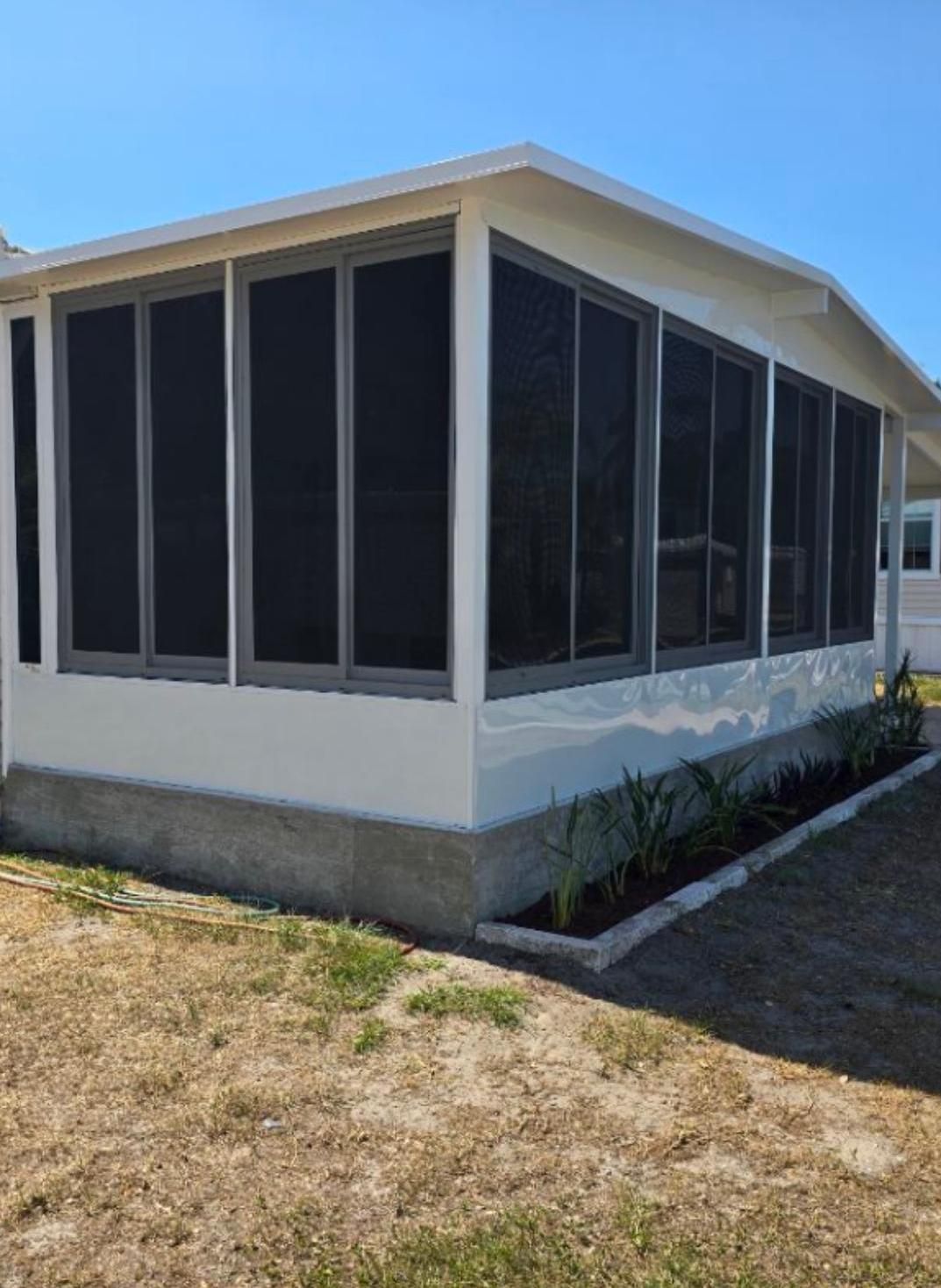 Screened-in porch with gray screens and white trim on a concrete base with landscaping in front.