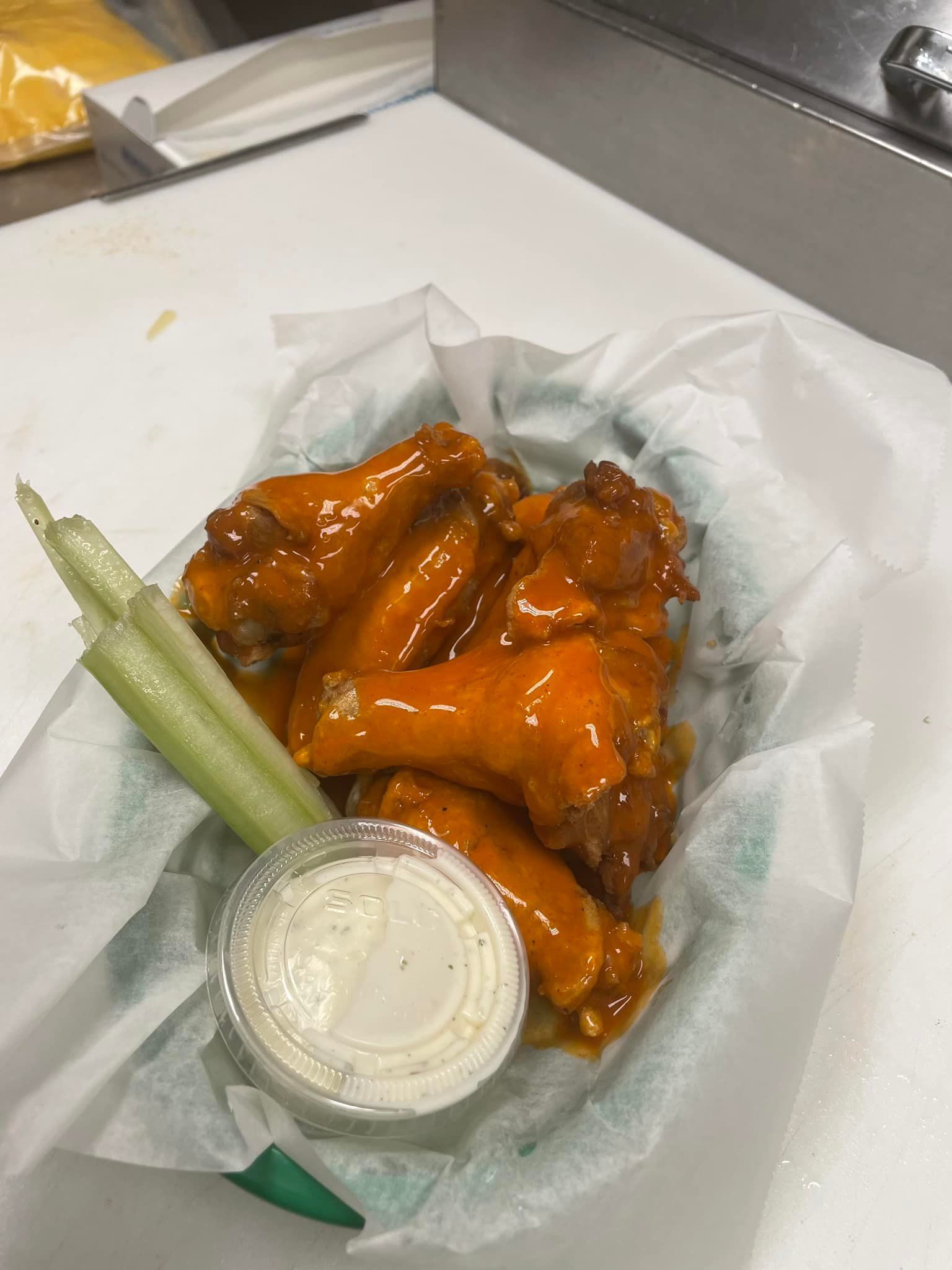 A basket of buffalo wings with celery and ranch dressing on a table.