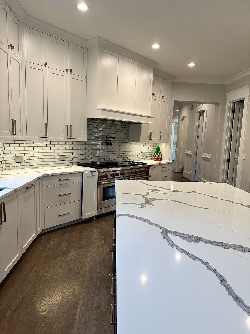 A kitchen with white cabinets, granite counter tops, a stove, and a large island.