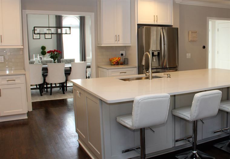 A kitchen with white cabinets, a large island, stools, a refrigerator and a sink.