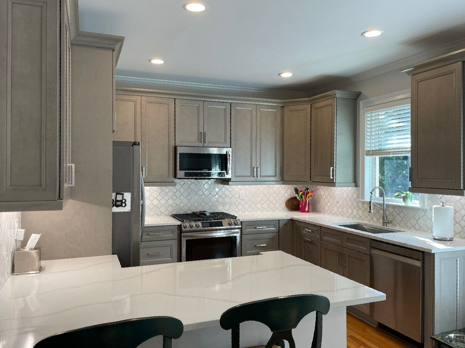 A kitchen with gray cabinets, white counter tops, stainless steel appliances and a large island.