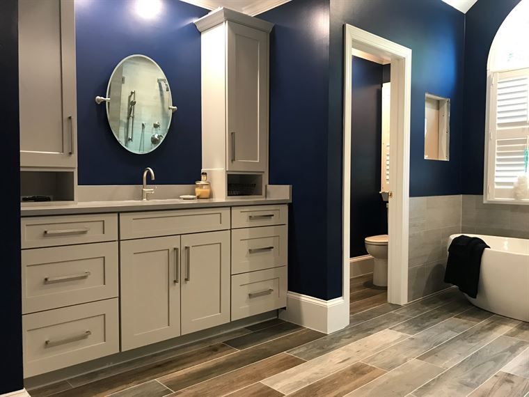 A bathroom with blue walls, white cabinets, a tub and a mirror.