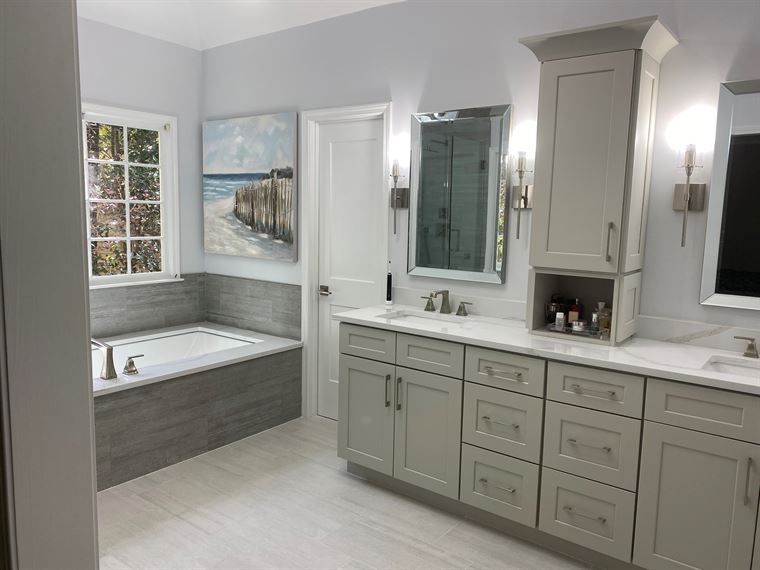 A bathroom with a tub, sink, mirror and cabinets.