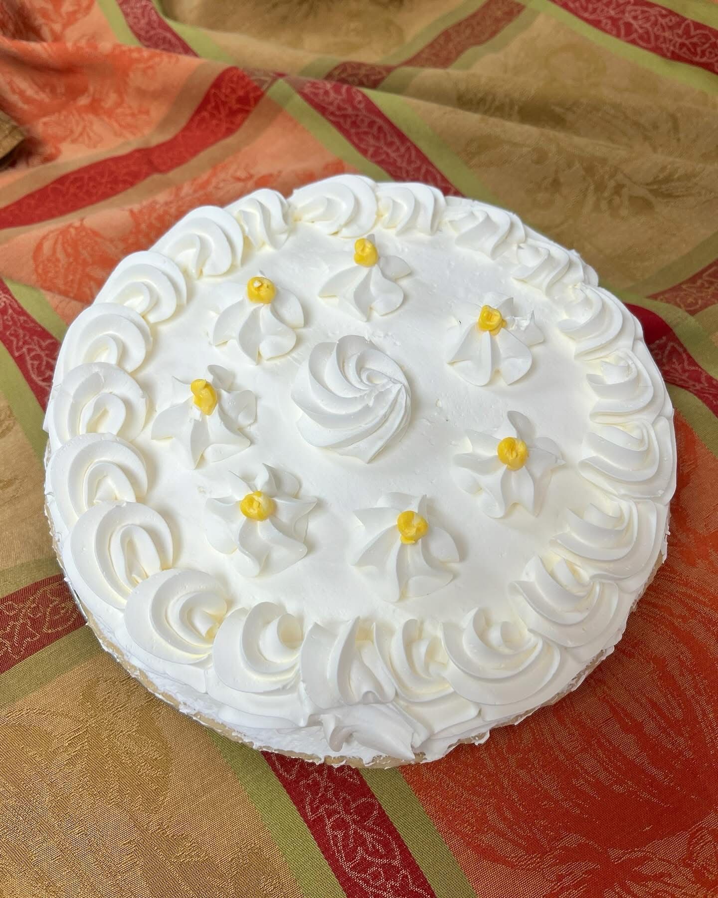 White frosted round cake with piped floral decorations on a patterned tablecloth.