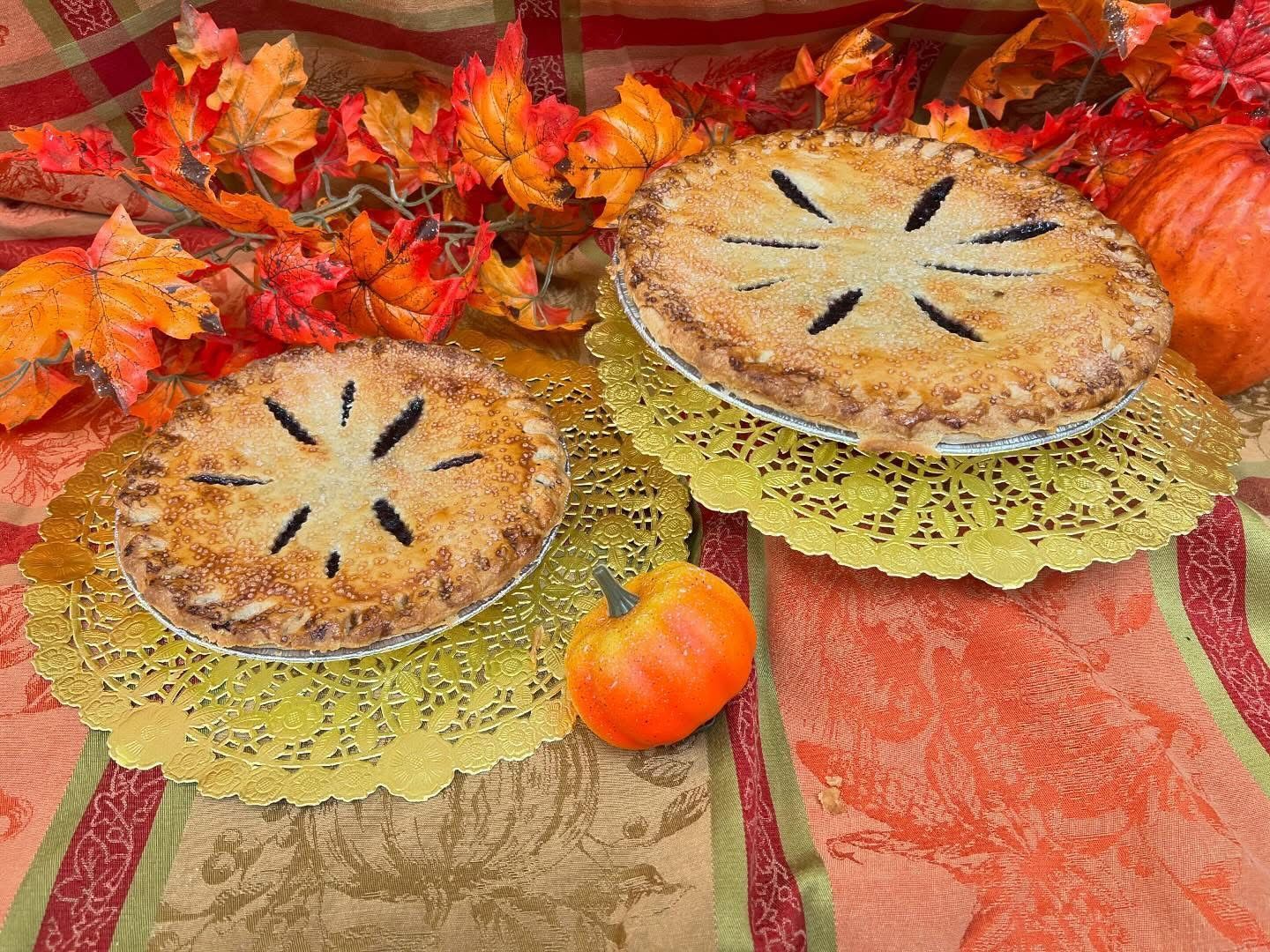 Two baked pies on gold doilies, with autumn leaves and a pumpkin on a patterned surface.