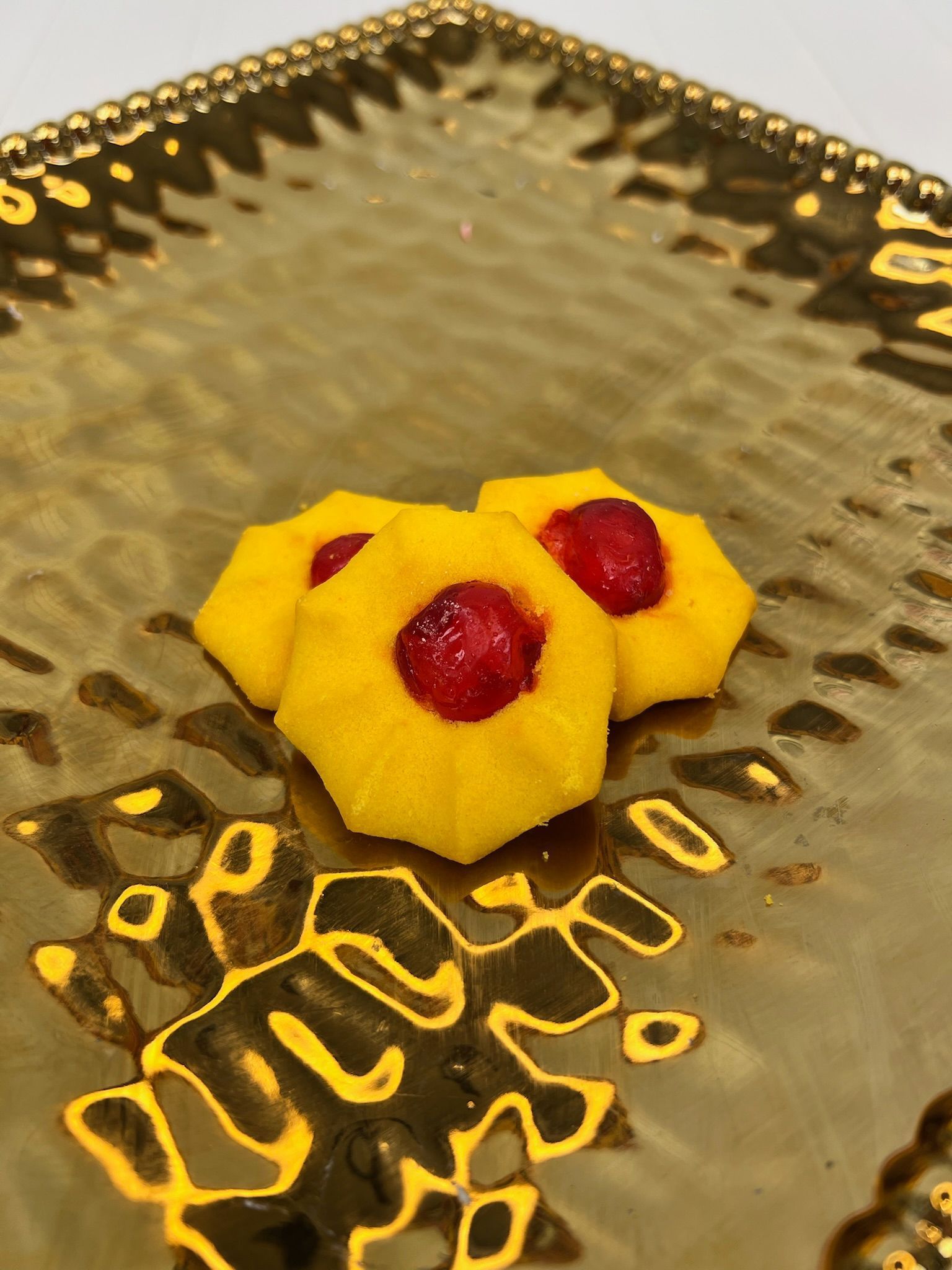 Three yellow cookies with red centers on a gold textured platter.