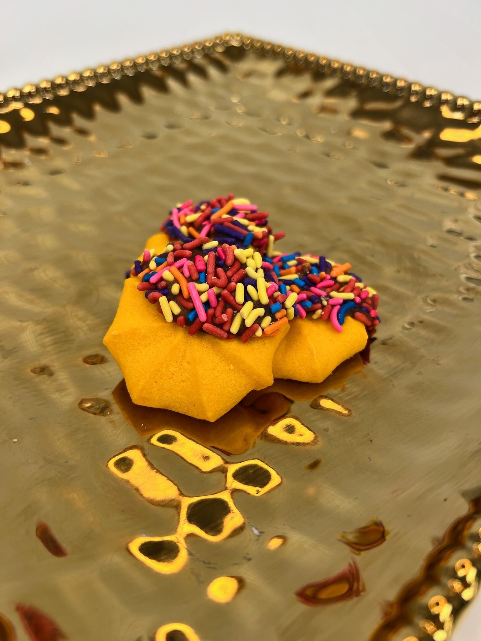 Two star-shaped cookies with rainbow sprinkles on a gold platter.