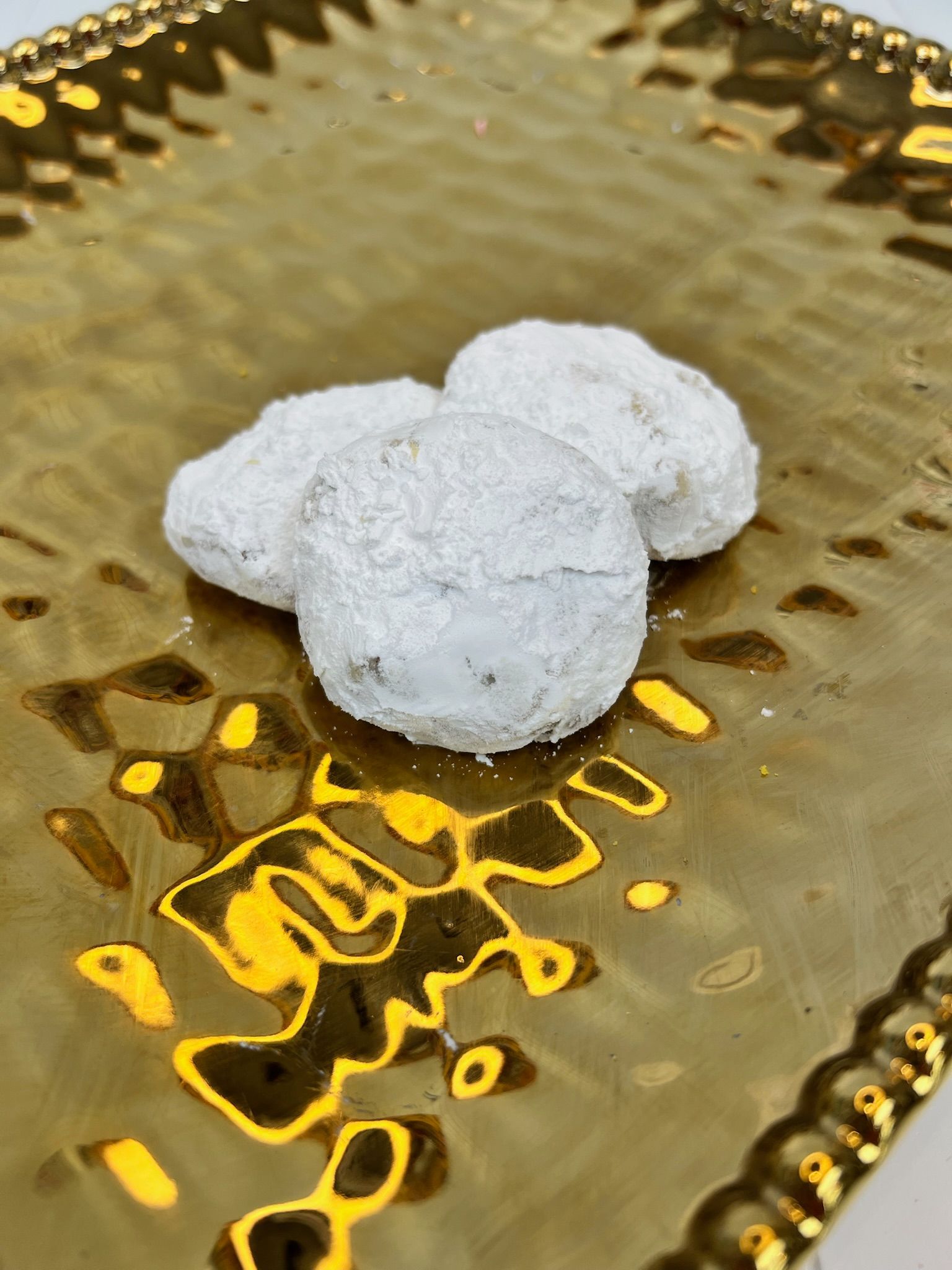 Three snowballs cookies on a gold-colored, textured, square serving platter.