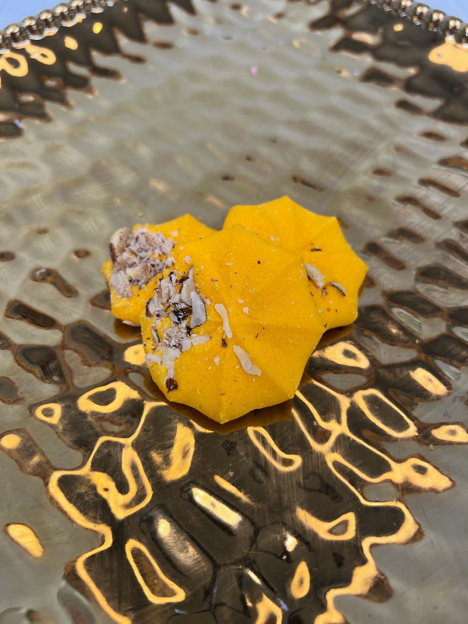 Yellow, flower-shaped dessert with topping on a textured gold plate.