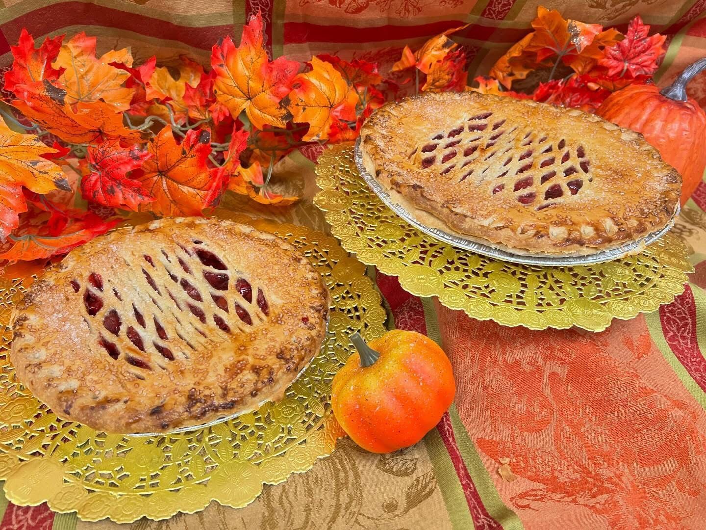 Two lattice-topped pies on doilies with autumn leaves and a small pumpkin.