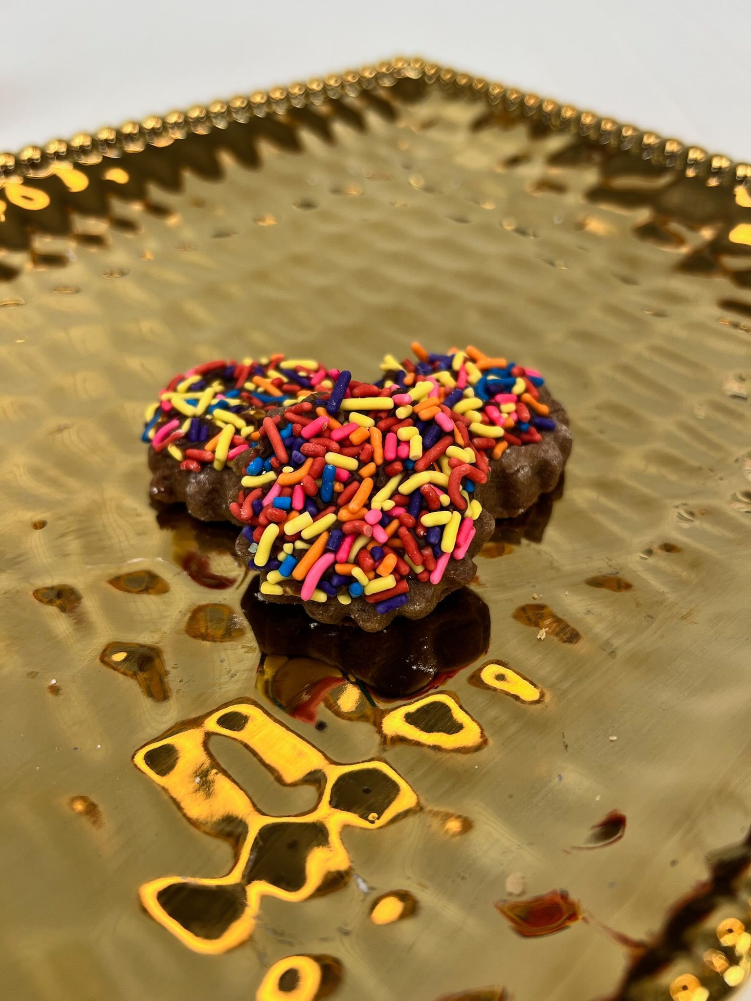 Heart-shaped cookies with colorful sprinkles on a gold textured plate.