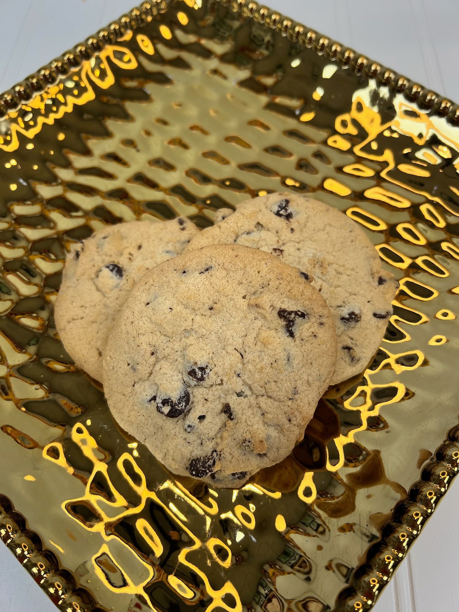 Three chocolate chip cookies on a gold, patterned plate.