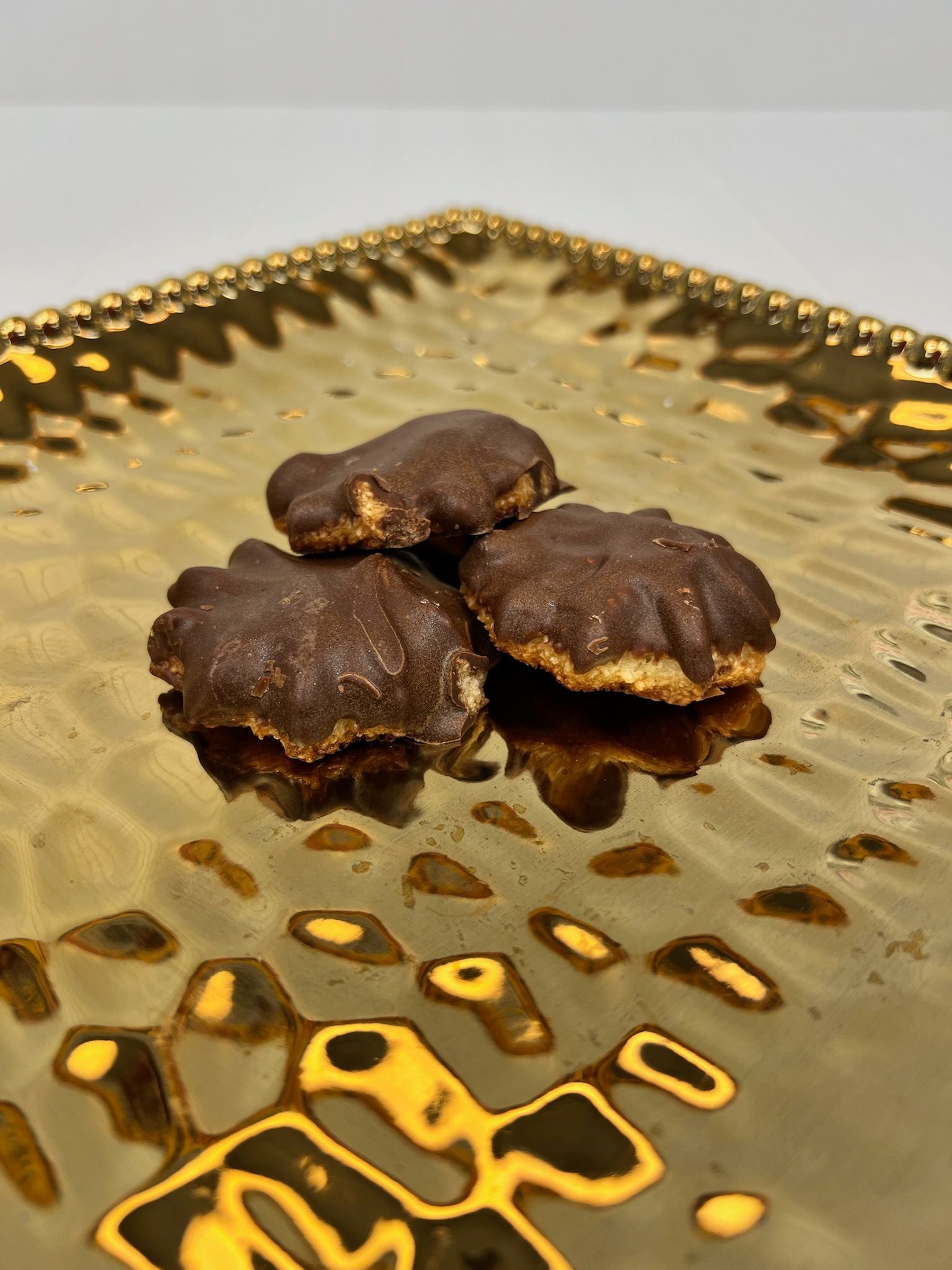 Three chocolate-covered cookies on a textured, gold-colored plate.